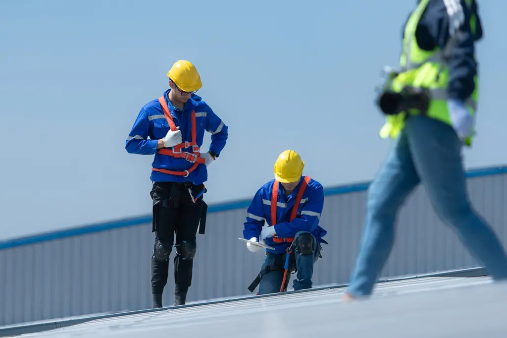 Professional team of workers in safety gear conducting commercial roof cleaning and maintenance on industrial building with proper fall protection equipment