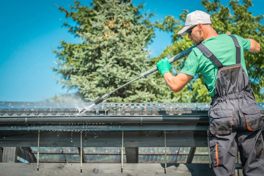 Worker cleaning residential gutter with pressure washer, showing gutter maintenance service