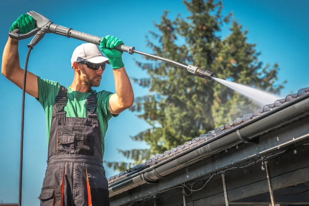 Professional roof cleaner using high-pressure washer on residential roof tiles with clear blue sky