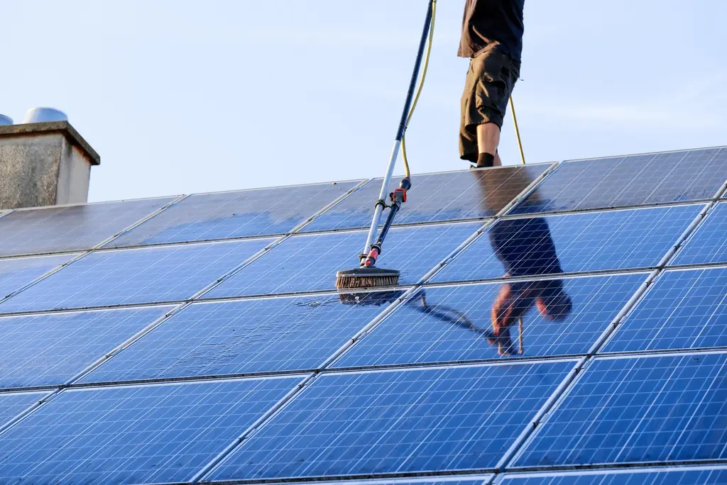 Professional worker cleaning solar PV panels on residential roof to maximize energy efficiency